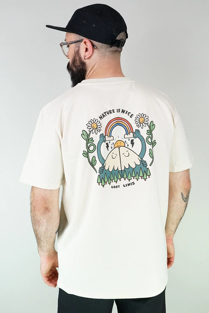 A man stands with his back to the camera, wearing a baseball bat, a white t-shirt with a colourful back print and black trousers. The design on the shirt is 2 mountains with smiling faces hugging. Above them is a smiley sun, above which the mountains are holding up a rainbow. Either side of this are two smiling daisies. Above the image are the words 'Nature is nice'.