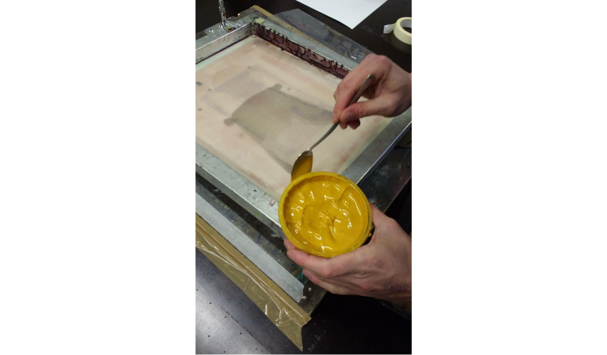A person is loading yellow ink onto a screen for screen printing.