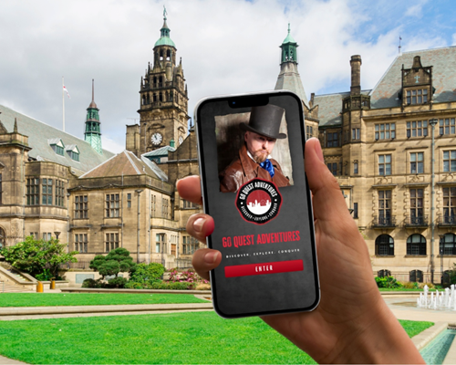 A smartphone being held up in front of Sheffield Town Hall and the Peace gardens, with a tour App on the screen.