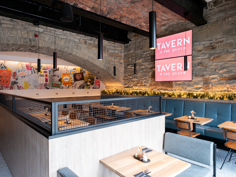 The interior of Tavern on The Quays, with bare stone walls and rows of tables and chairs.