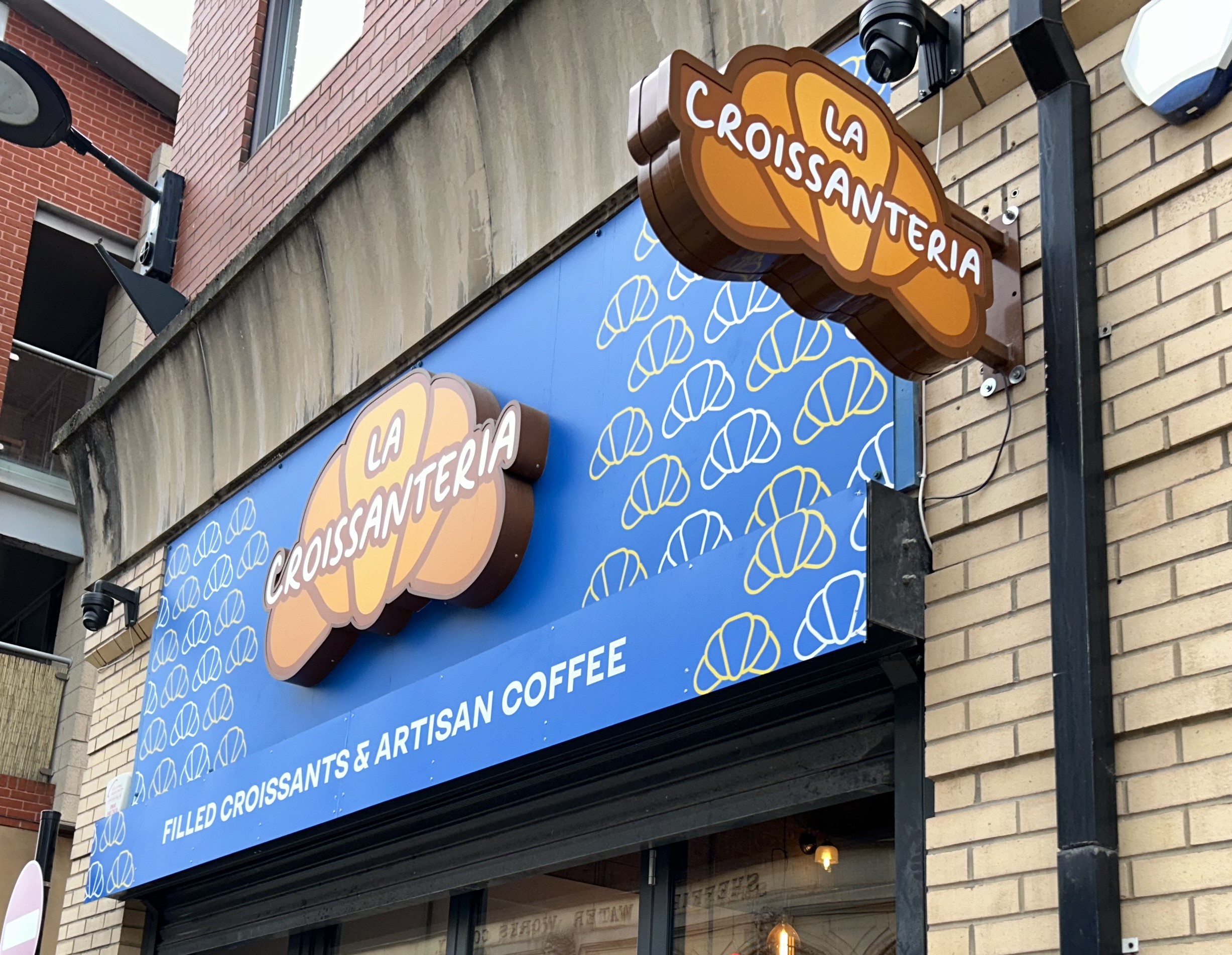 A side view of the sign outside of the shop, which reads La Croissanteria, the title is placed on top of croissant 