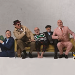 The band Madness all piled on to and around a yellow sofa.