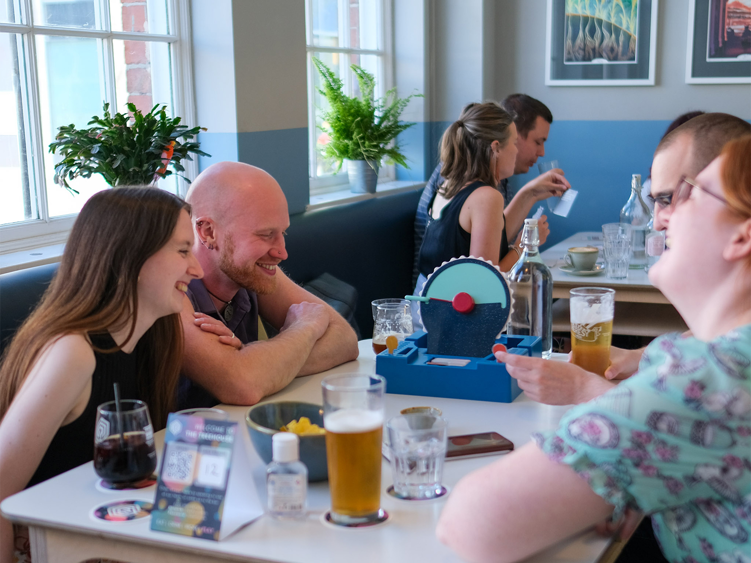 Two tables at The Treehouse Cafe, both filled with people enjoying drinks and playing board games.