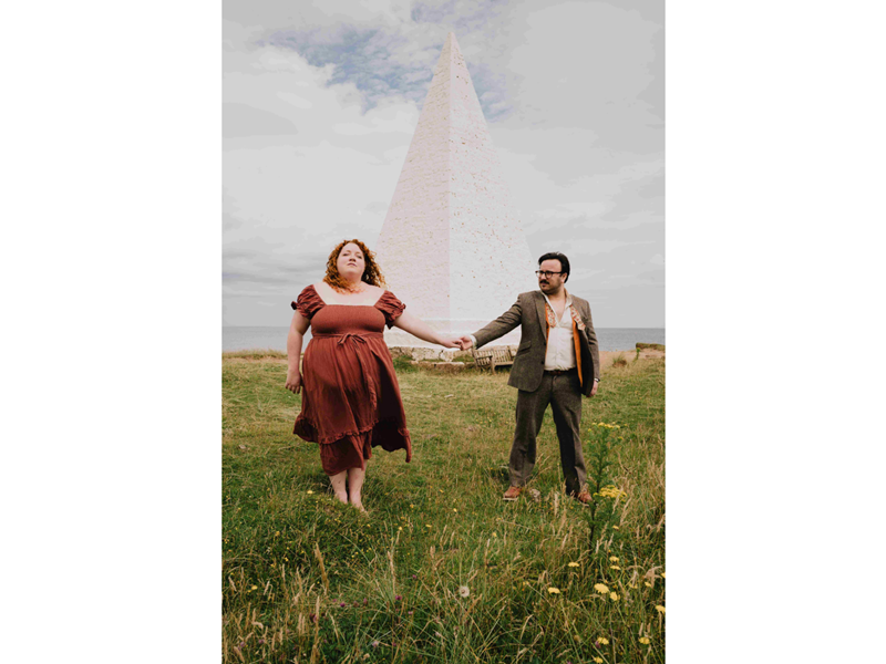 Will Finn and Rosie Calvert standing in a field in front of an obelisk.