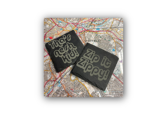 Two black coasters with bold white text placed on a detailed map of Sheffield. One coaster reads 'Tha's nesh kid!' and the other reads 'Zip it Zippy!'. The map beneath shows streets and landmarks, providing local context to the Yorkshire phrases.