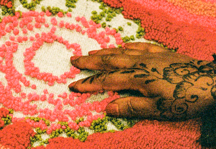A close-up of a hand working on a colourful rug.