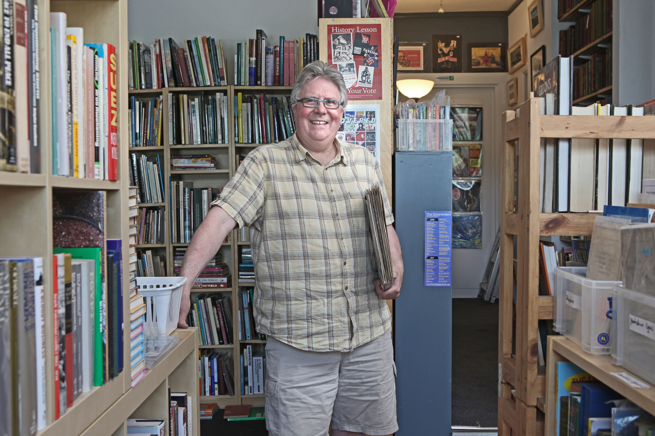 A man is smiling at the camera surrounded by shelves packed with books in the Kelham Books & Music shop.