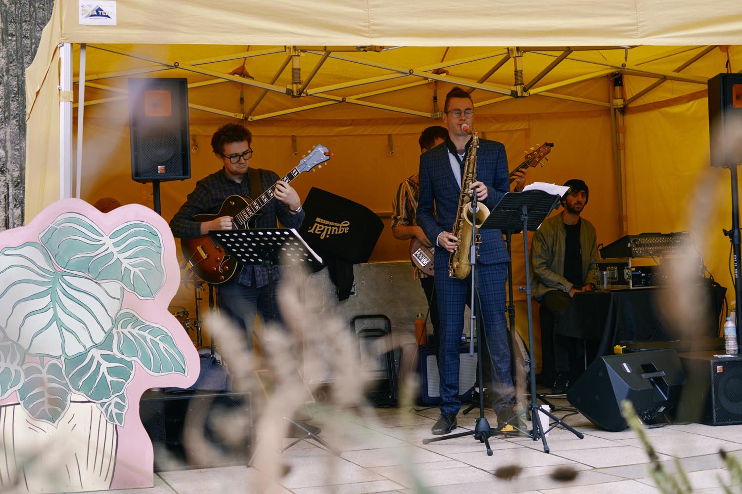 Band with a frontman playing the saxophone, guitarist and keyboard player in a yellow tent