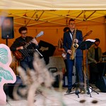 Band with a frontman playing the saxophone, guitarist and keyboard player in a yellow tent