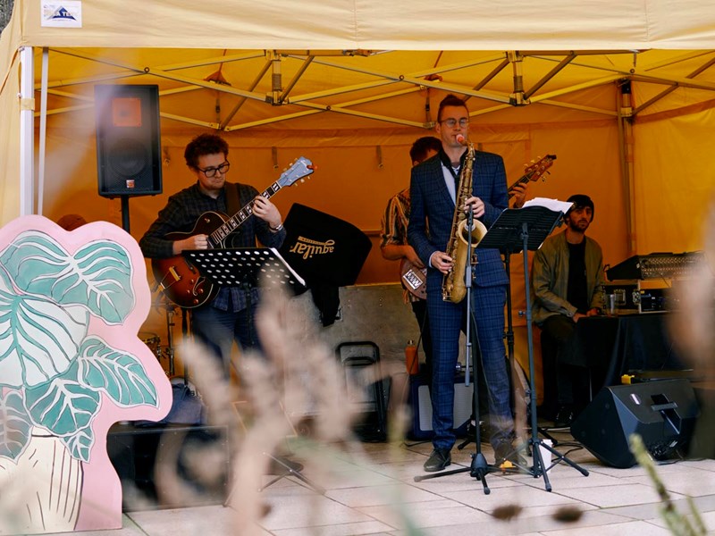 Band with a frontman playing the saxophone, guitarist and keyboard player in a yellow tent