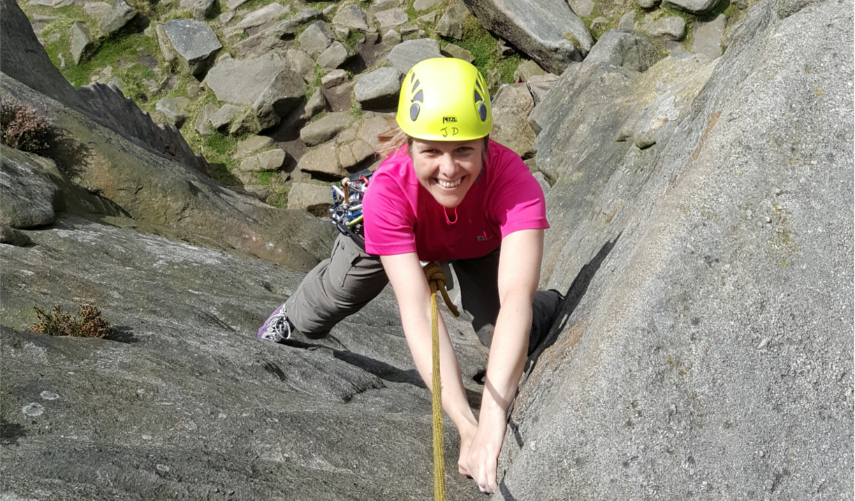 A woman climbing a rock face with a big smile on her face.