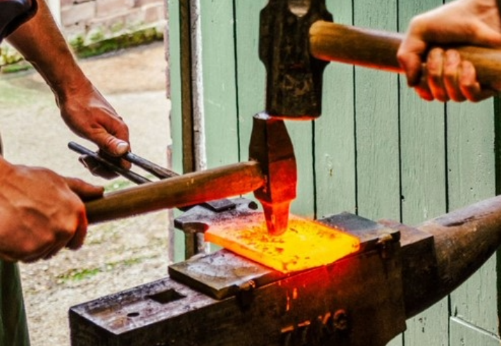 A close-up of two people forging a piece of metal on an anvil.