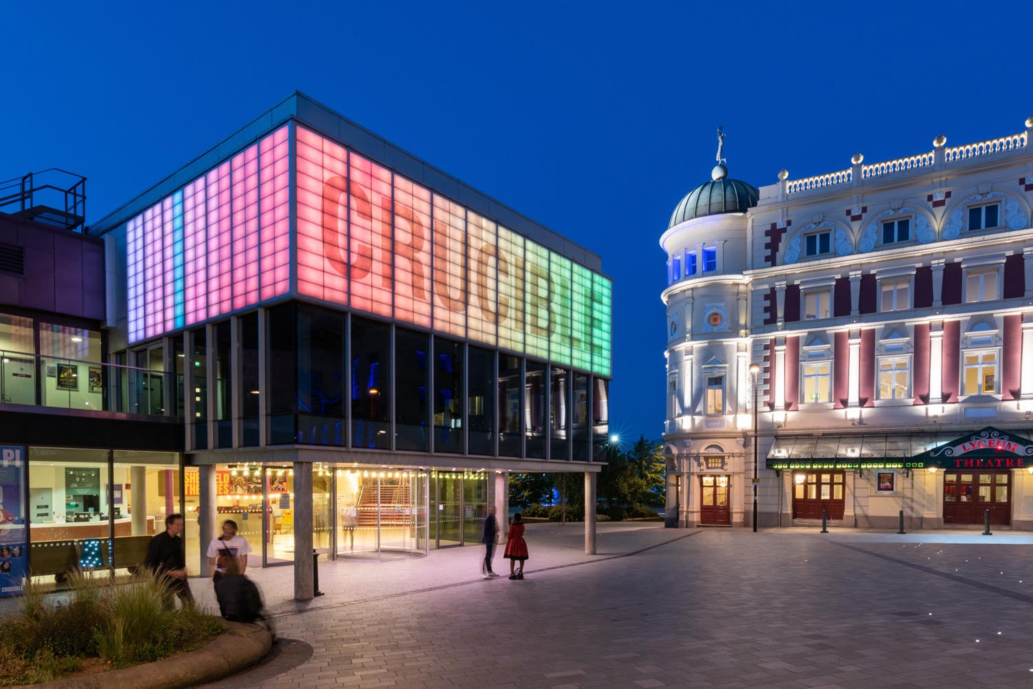 The Crucible and Lyceum Theatres, in Tudor Square in Sheffield, at dusk. Both buildings are well lit and look cheerful and inviting.