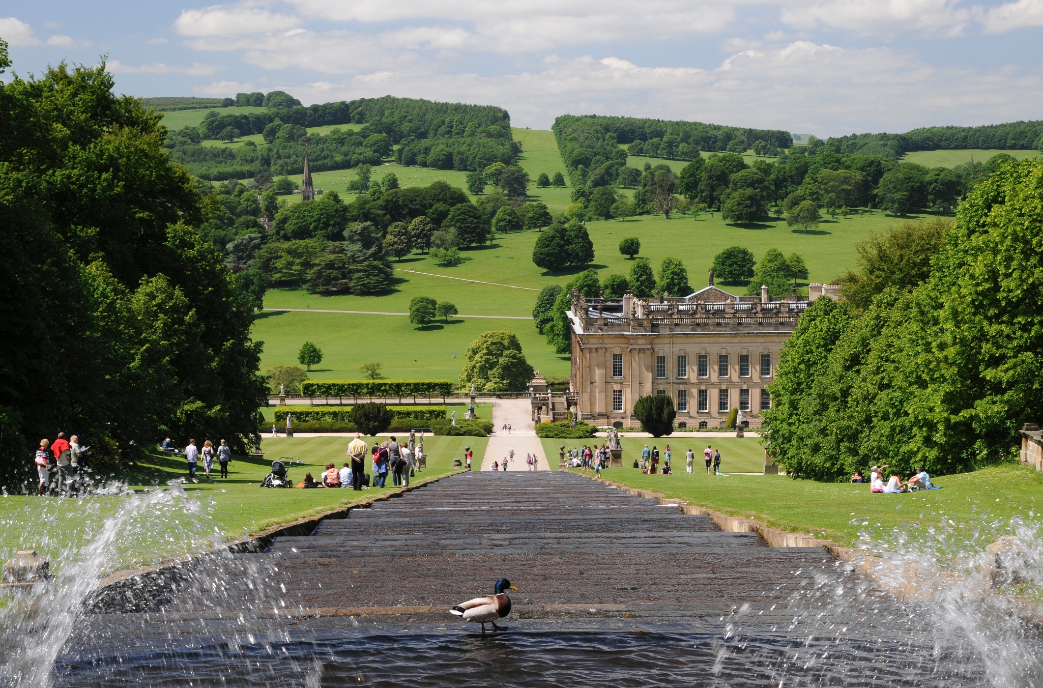 A water feature running down a hill with Chatsworth House in the distance.