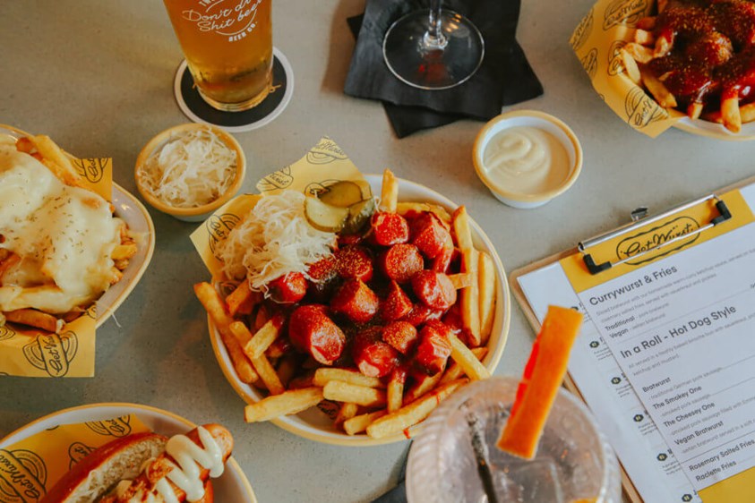 German street food with fries and frankfurters in a bowl surrounded by raclette dishes and beer