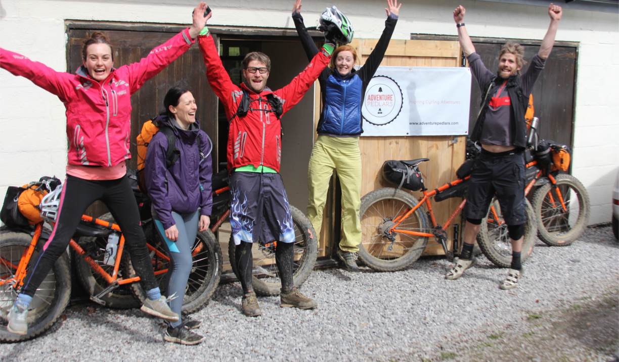 People cheering with their arms in the air, outside a building. There are several mountain bike lent up against the building.