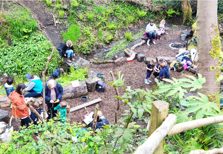 A group of people in a woodland clearing are taking part in a workshop.