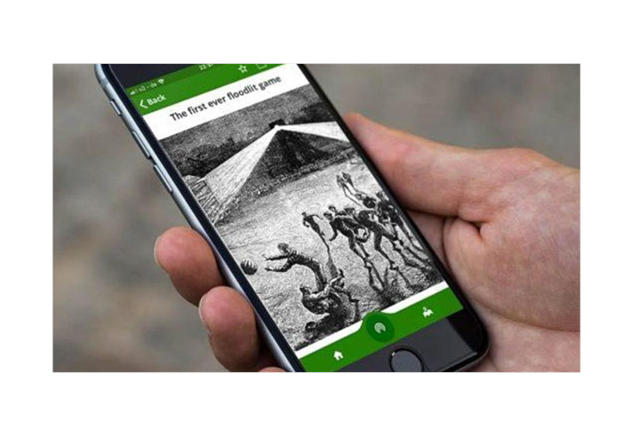 A hand holding a smart phone. On the screen is an App with a black and white image of people playing football.