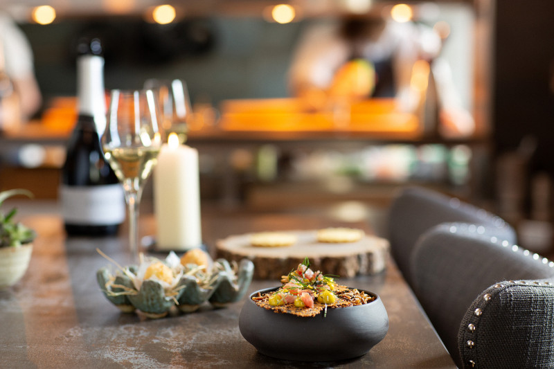 A table at a restaurant with small plates and bowls of food , a glass of wine and a candle.