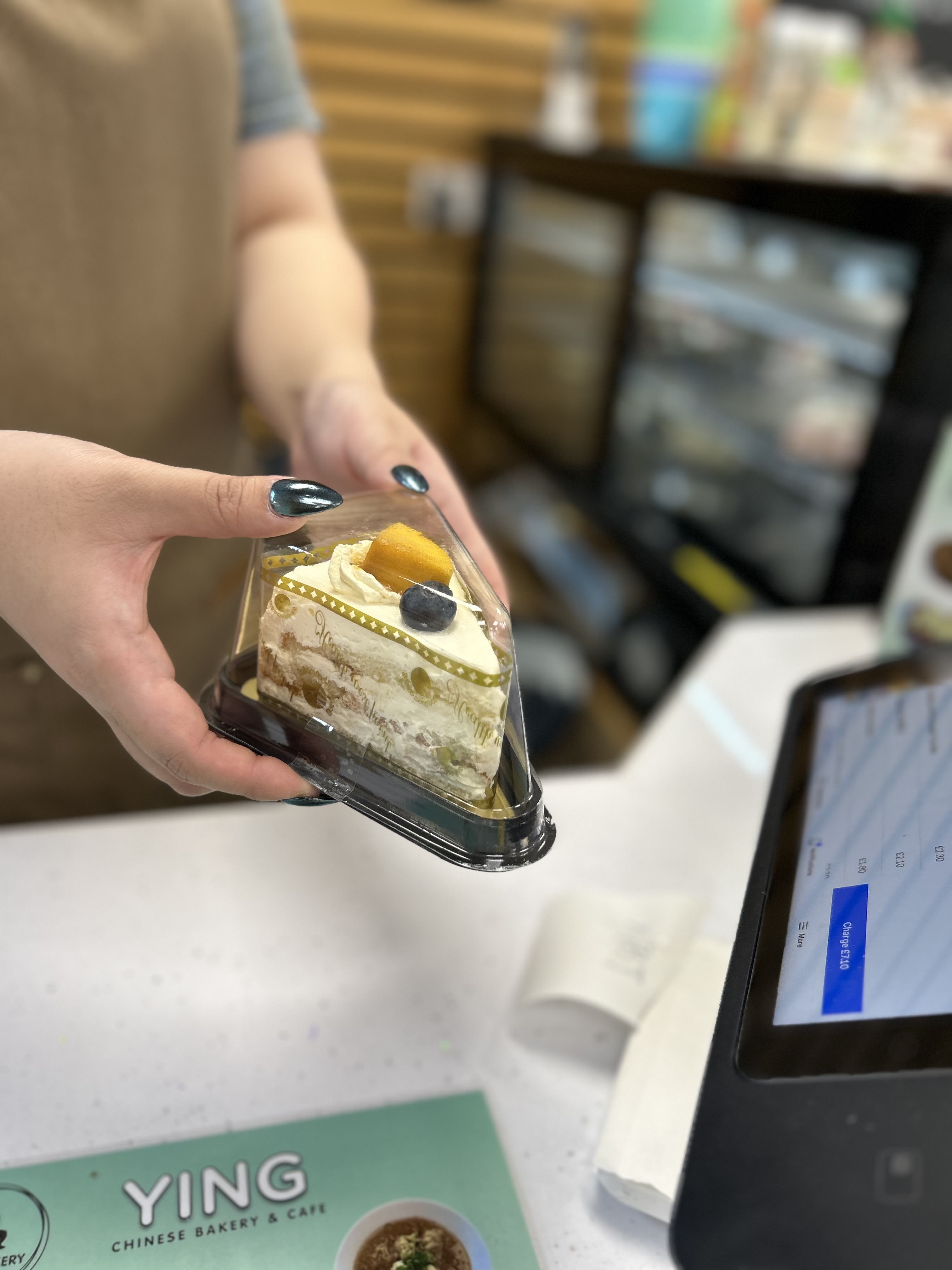 an image of someone's hands holding a triangle shaped transparent box which has a cream cake on the inside  