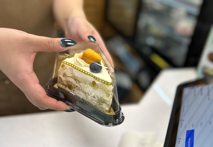 an image of someone's hands holding a triangle shaped transparent box which has a cream cake on the inside