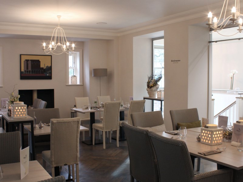 Restaurant and breakfast room with smart, modern set tables and cosy upholstered chairs.