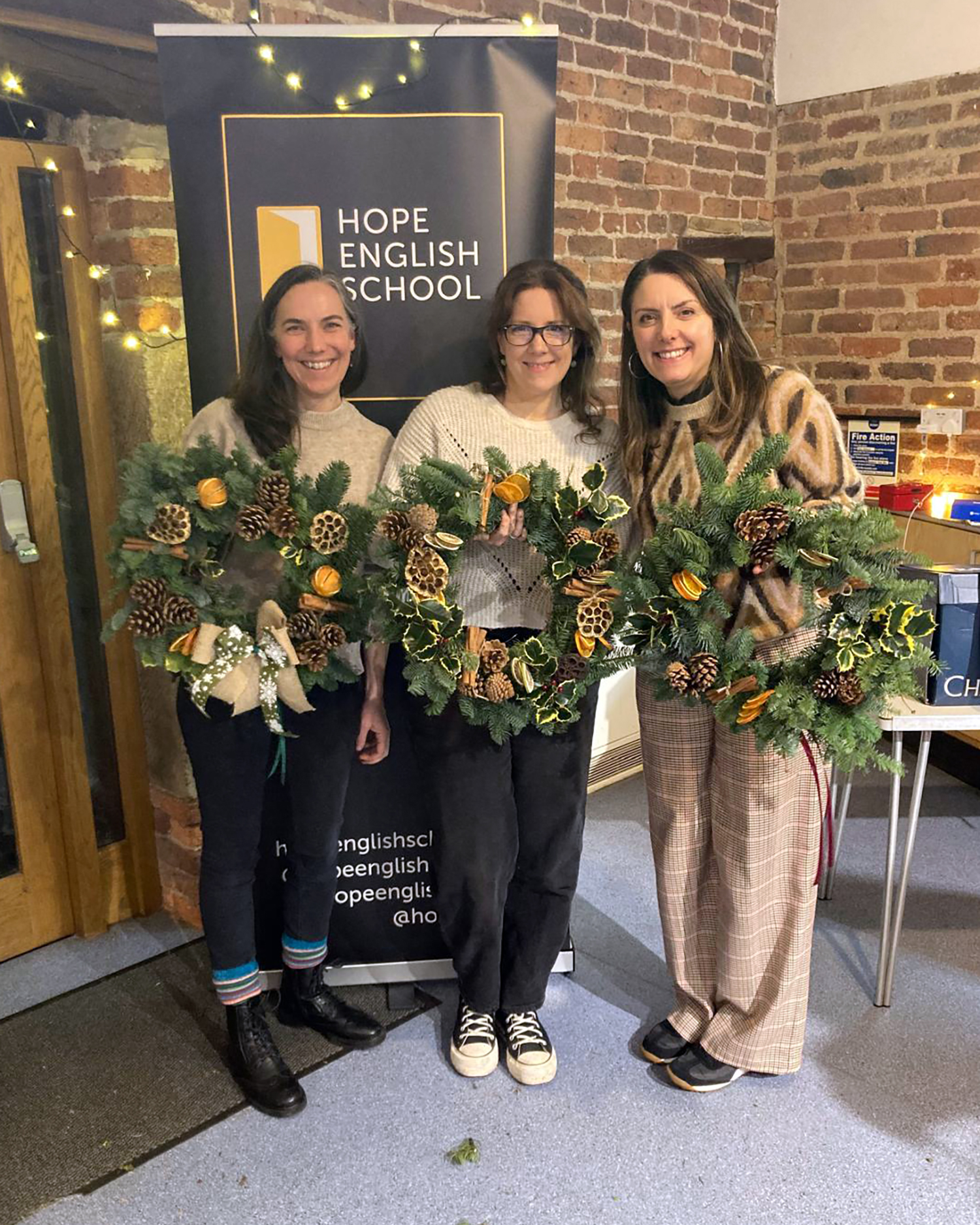 Three women proudly holding Christmas wreaths that they have made.