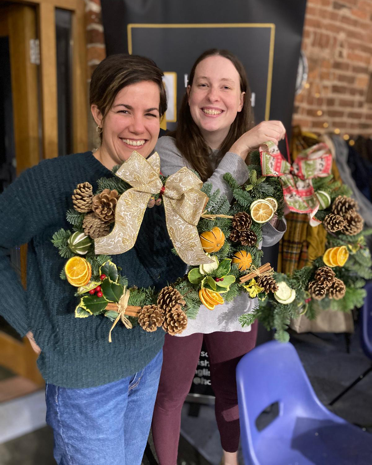Two women proudly holding Christmas wreaths that they have made.