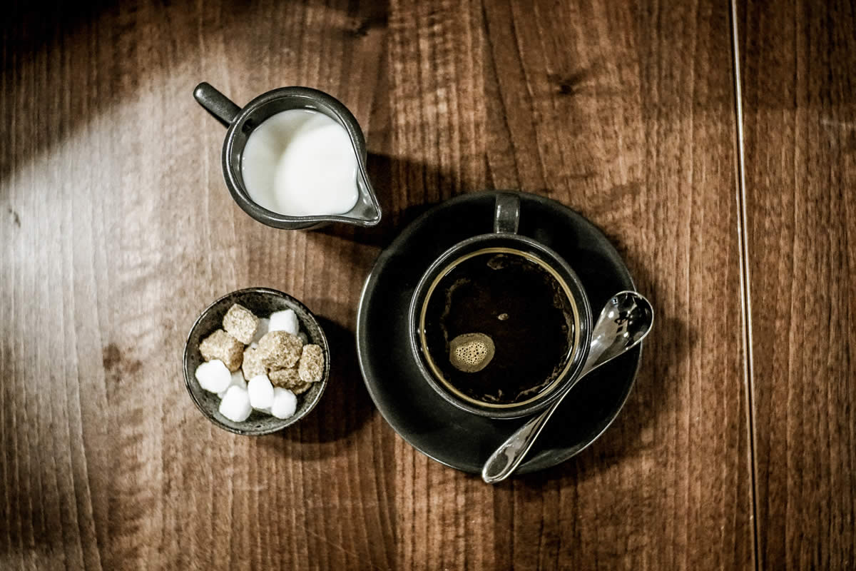 Overhead shot of a cup of coffee with a bowl of sugar cubes and a small metal jug of milk at Inox Dine.