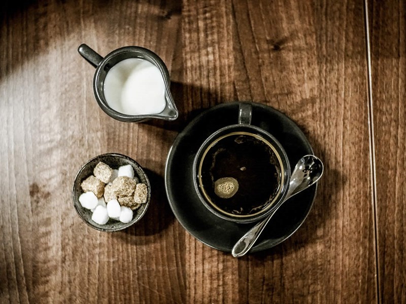 Overhead shot of a cup of coffee with a bowl of sugar cubes and a small metal jug of milk at Inox Dine.