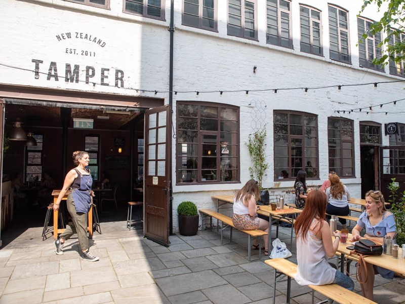 The courtyard at Tamper Coffee, with customers sat at tables.