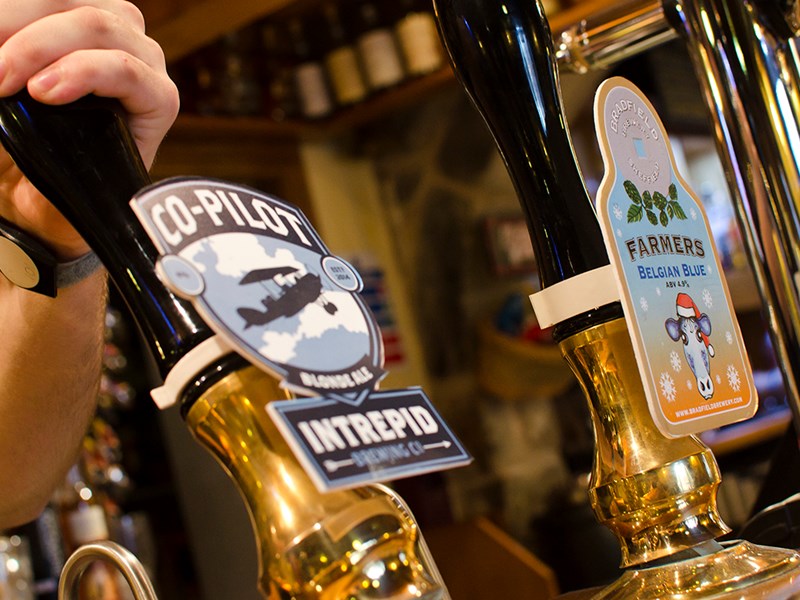 A hand pulling on a beer pump on a bar.