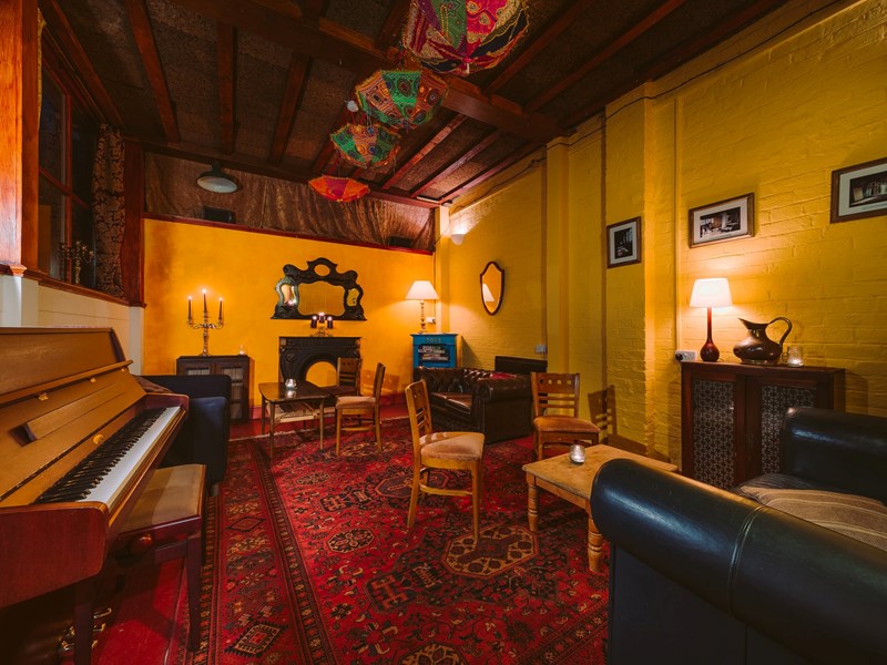 A room with a piano and a sofa and chairs around a low table.