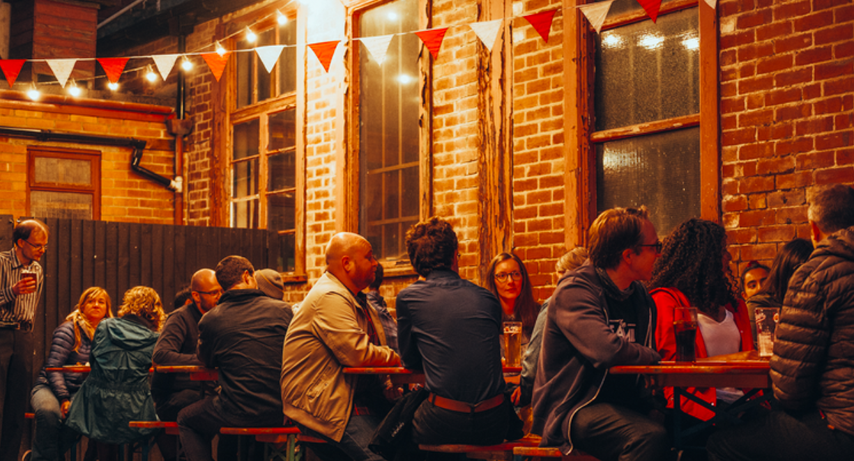 A group of people sat at tables outside, at night, having a night out. 