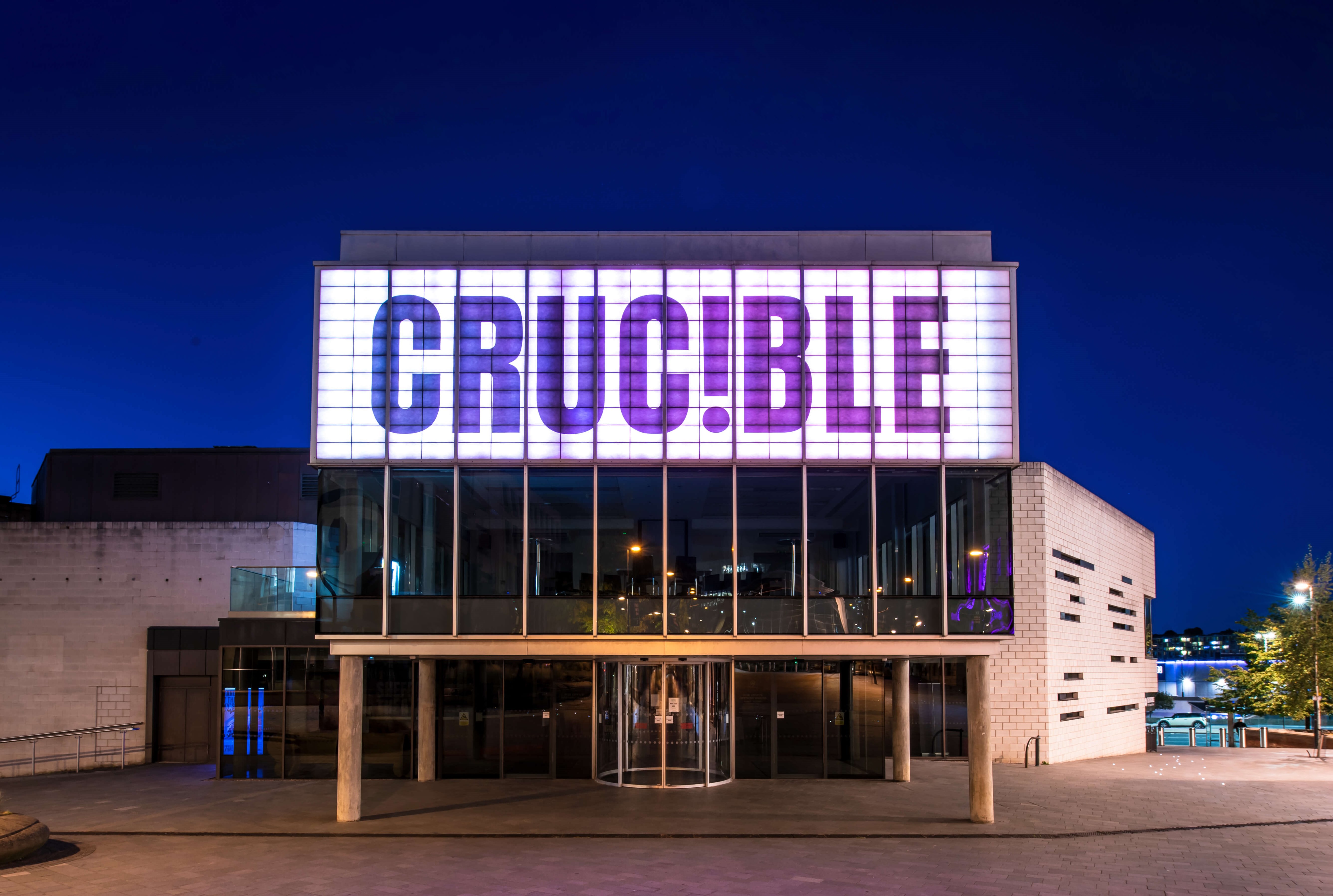 The exterior of the Crucible Theatre at night, with its illuminated sign, as seen from Tudor Square.