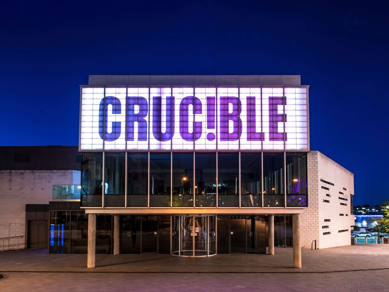 The exterior of the Crucible Theatre at night, with its illuminated sign, as seen from Tudor Square.