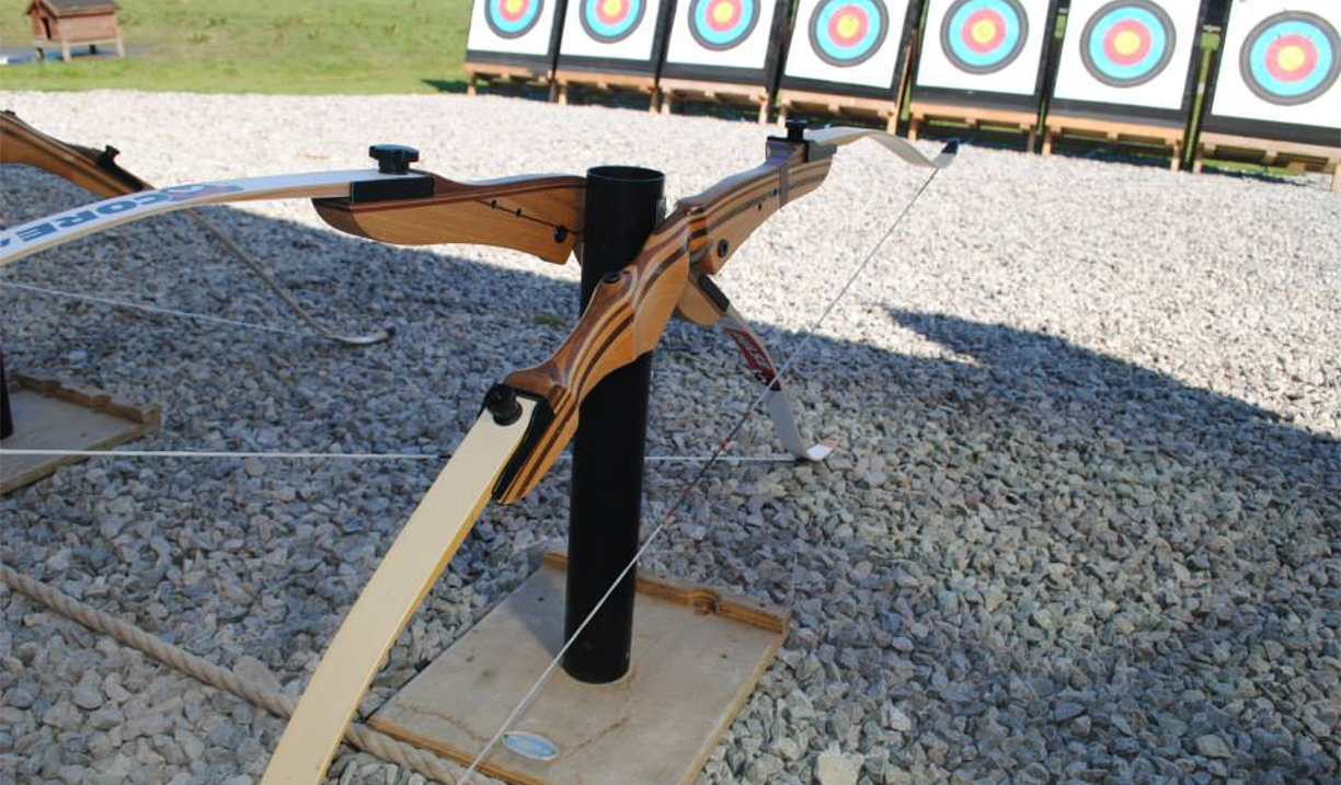 Two bows on a stand, in the distance is a row of archery targets.