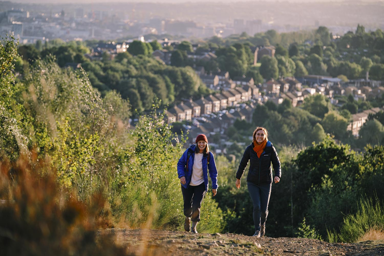 Two people walking in the hills above Sheffield. In the distance you can see rows of houses and the city skyline.