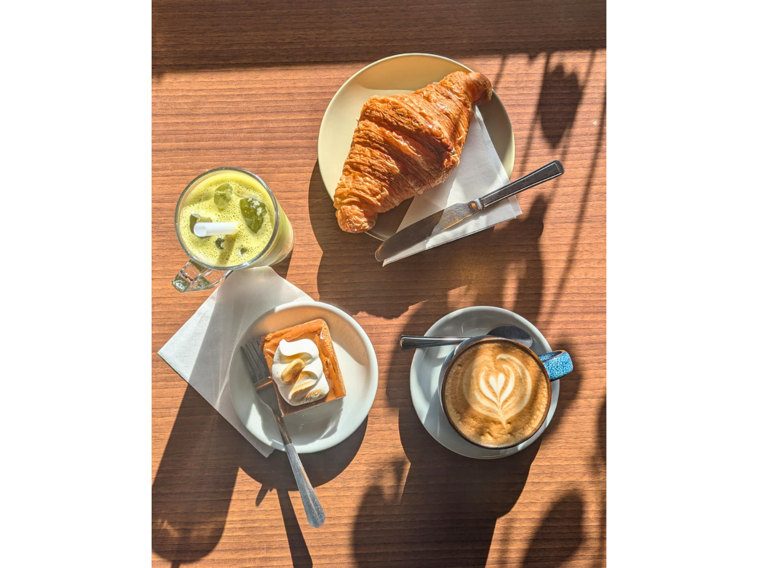 A wooden table, in the sun, with a coffee, delicious pastries and a smoothie at the Copper Pot Café.