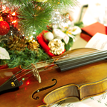 A violin on a table covered in sheet music and a Christmas ornament off to one side.