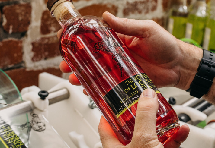 Two hands holding a bottle of Locksley gin that is red in colour.