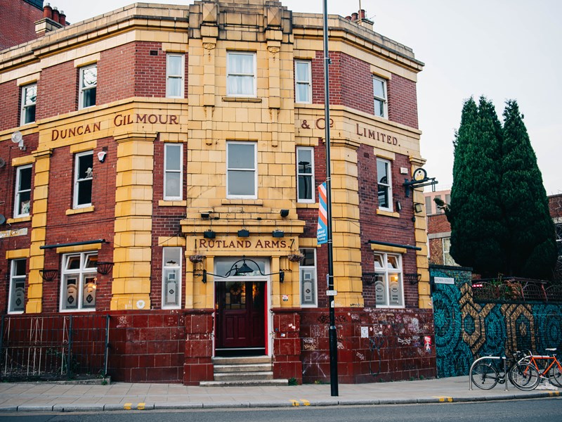 Rutland Arms exterior. The building is red and mustard brick, with grey sky in the background and two bicycles and street art to the right of the building.