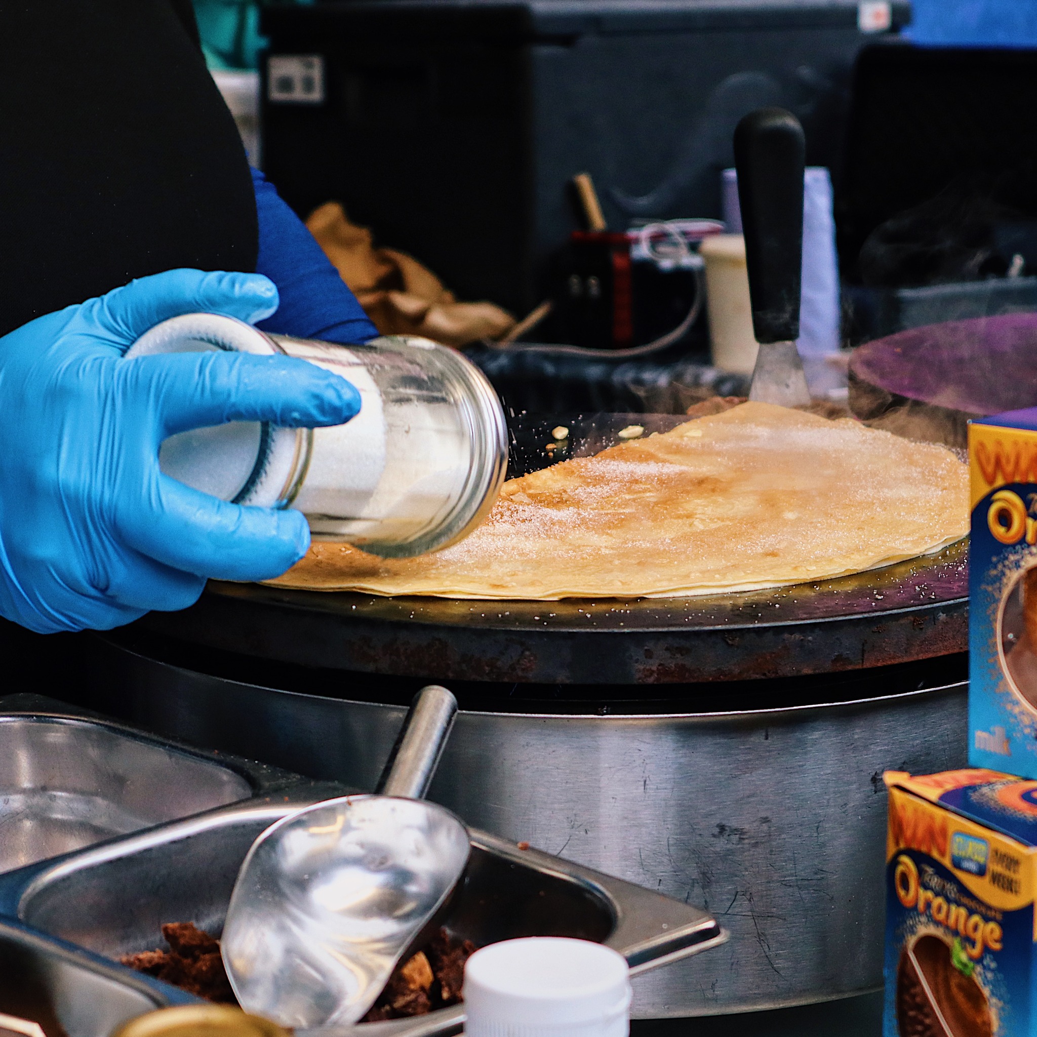 A stall trader is shaking sugar on a fresh crepe.