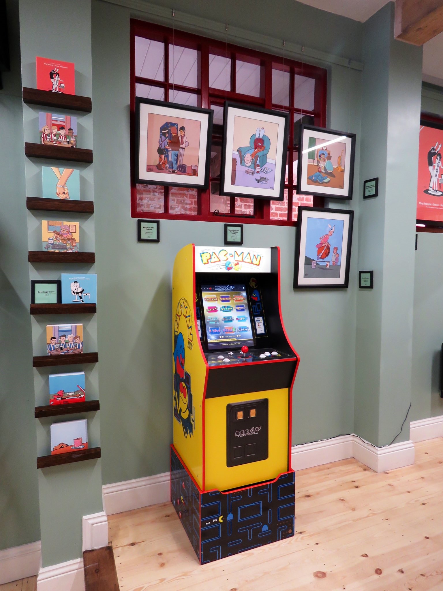 A Pac-Man arcade machine in the Pete Mckee Gallery, surrounded by prints on the wall.