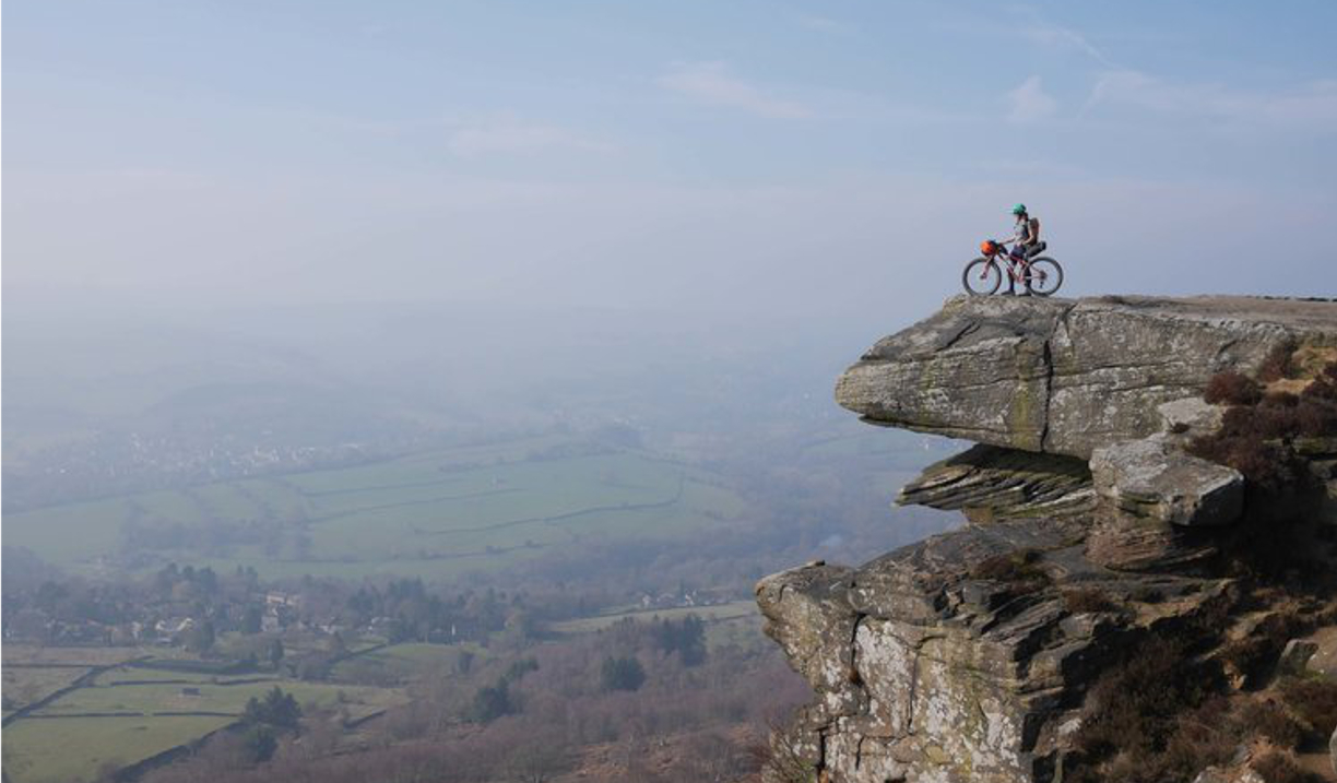  A person, on a mountain bike, on top of a rocky outcrop.