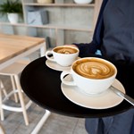 Two cappuccinos being carried on a tray.