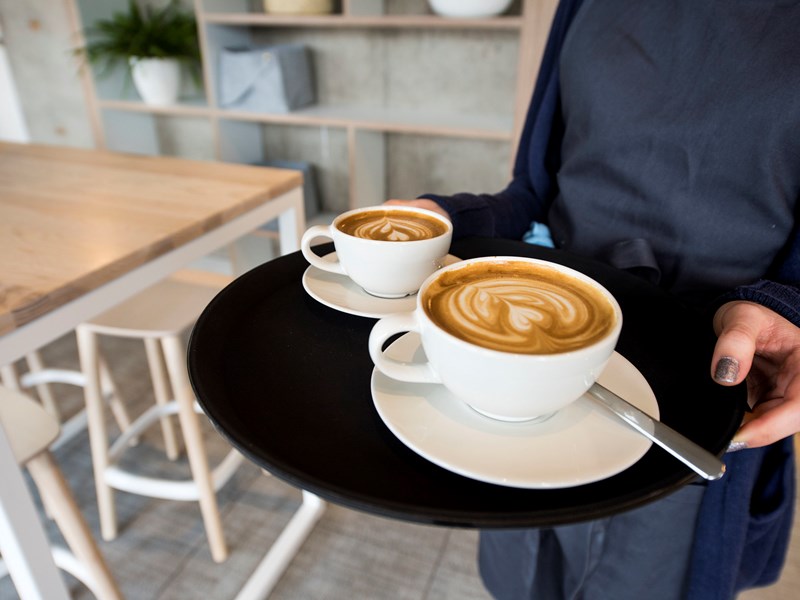 Two cappuccinos being carried on a tray.