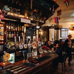 Rutland Arms interior. The bar is at the forefront, with groups of people in the background sat talking at drinking.