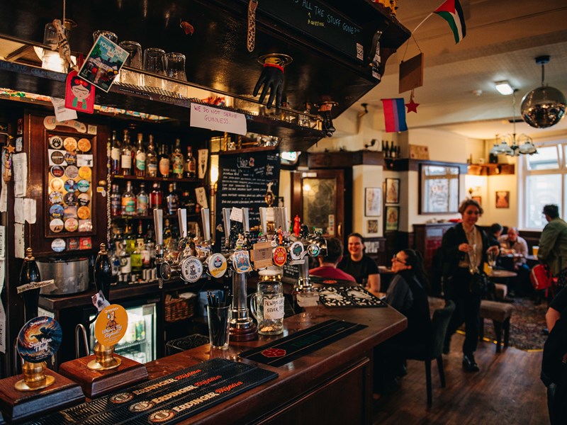 Rutland Arms interior. The bar is at the forefront, with groups of people in the background sat talking at drinking.