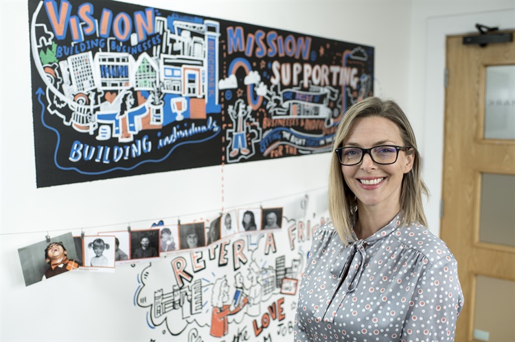 A smiling woman stands in front of a wall that is filled with information posters.